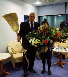 Премиерът държи метла опасана с националния трибагреник, подарена му от чистачките на летище София, които лично спаси от уволнение. 