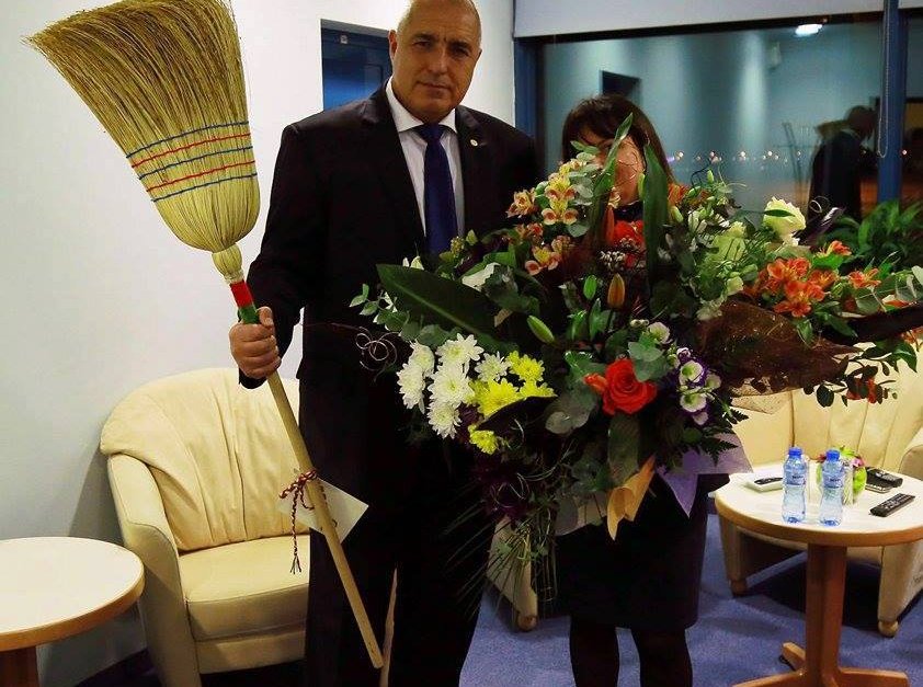 Премиерът държи метла опасана с националния трибагреник, подарена му от чистачките на летище София, които лично спаси от уволнение. 