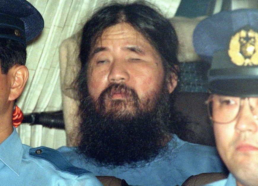 Шоко Асахара ескортиран от двама полицаи през септември 1995 година.