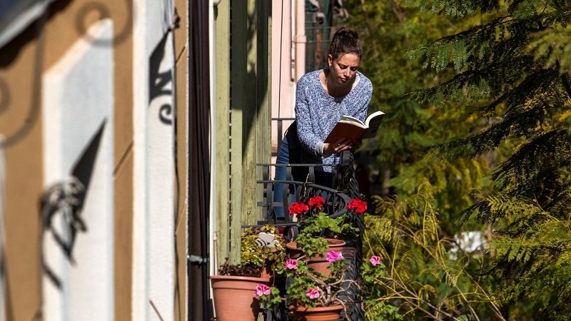 Млада жена чете книга на балкона си в Баарселона по време на карантината за коронавируса.