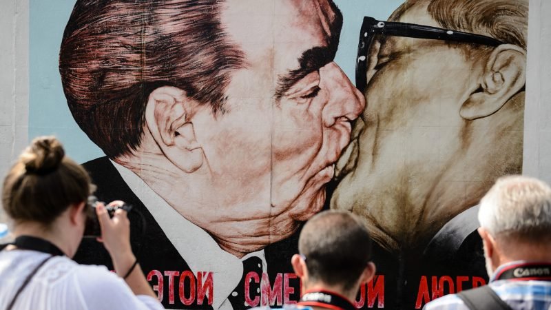 Туристи разглеждат картината-графит "Боже мой, помогни ми да преживея тази смъртоносна любов" на художника Дмитрий Врубел на участък от бившата Берлинска стена, в Берлин. Произведението на изкуството, известно още като "Братска целувка" (Bruderkuss на немски) изобразява целуващите се комунистически лидери Леонид Брежнев от Съветския съюз и Ерих Хонекер от ГДР.  Снимка: ЕПА/БГНЕС